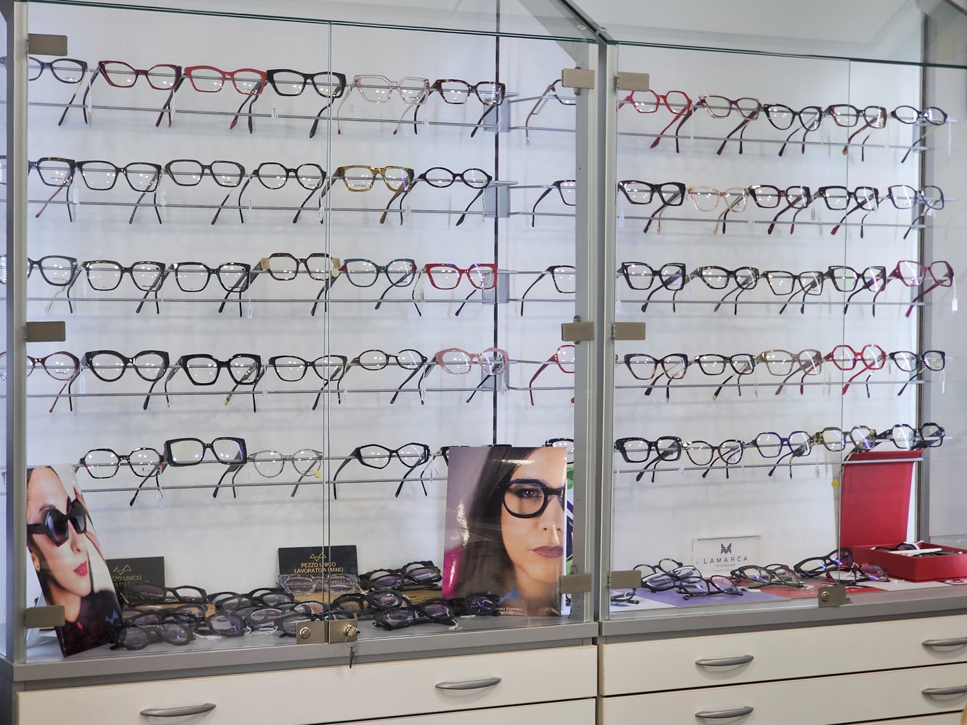 Vetrine in vetro di Ottica Medical con montature colorate su barre, cassetti bianchi sotto e cartello Lamarca